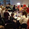 Till höger: Kateryna Blagodyr, grundare Help Ukraine Gothenburg, julmarknad, Ukraina, hjälporganisation. Till vänster: Barn och vuxna står och pysslar julklappar vid ett bord. Flera har tomteluvor på sig.
