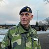 Regementeschefen Per Åkerblom, man klädd i militärkläder, tittar snett in mot kameran. Militära fordon i bakgrunden.