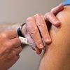 En bild på en spruta med vaccin mot covid 19 som sätts i överarmen på en man.