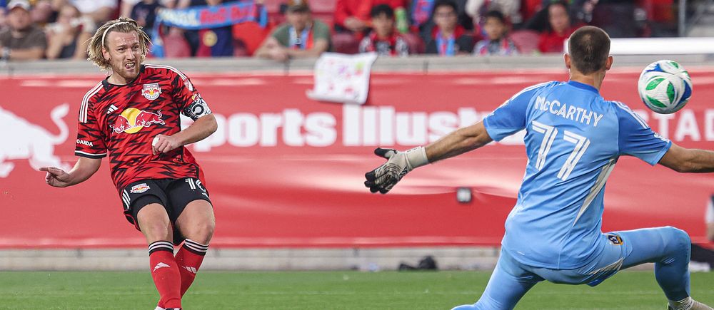 Fotbollsspelare skjuter mot mål medan målvakten försöker rädda med utsträckta armar.