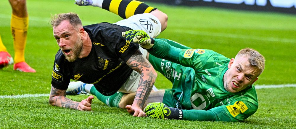 Fotbollsspelare och målvakt kolliderar och faller till marken under en match på gräsplan.