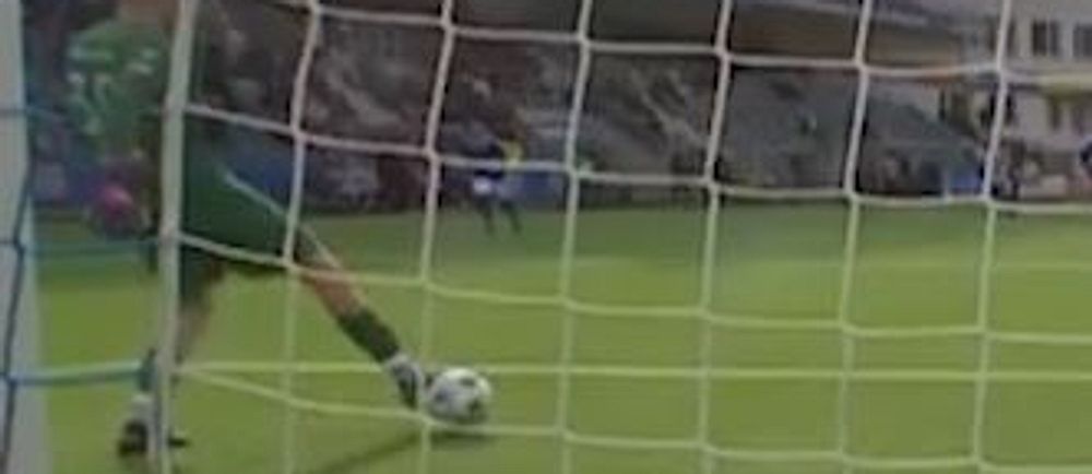 Målvakt sparkar boll vid fotbollsmål under match, publik synlig i bakgrunden.