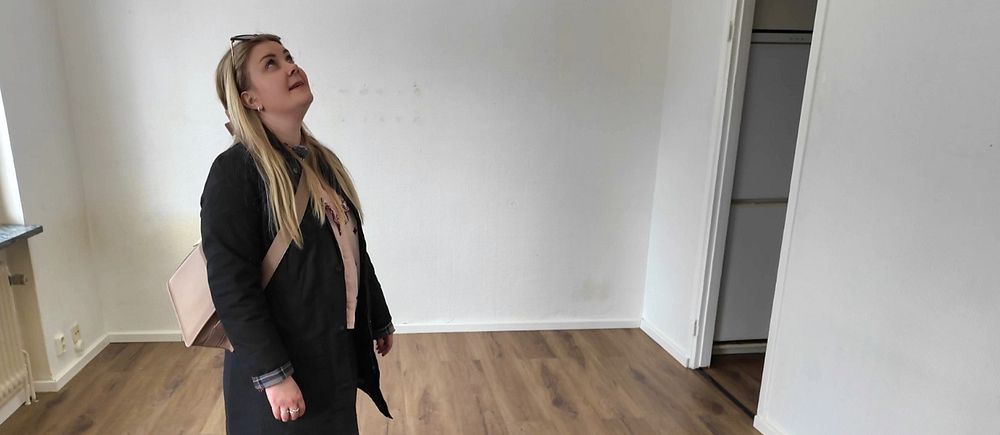 Rebecka Perä undersöker interiören i ett tomt rum med trägolv och vitmålade väggar.