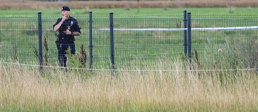 En polis står bakom ett staket med högt gräs i förgrunden. Händelsen utspelar sig i Hyllinge i Åstorps kommun.