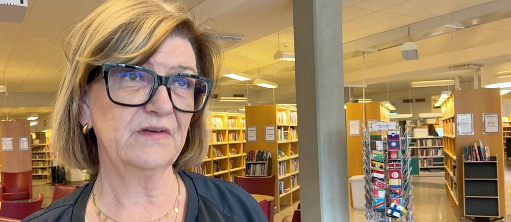 Person med blont hår framför bokhyllor i ett bibliotek.
