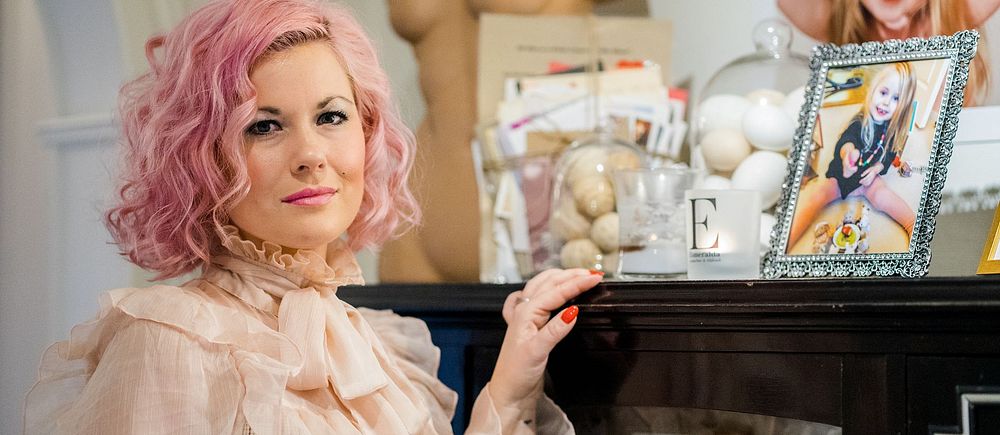 Melinda Jacobs sitter vid ett bord med inramade foton och prydnader i bakgrunden.