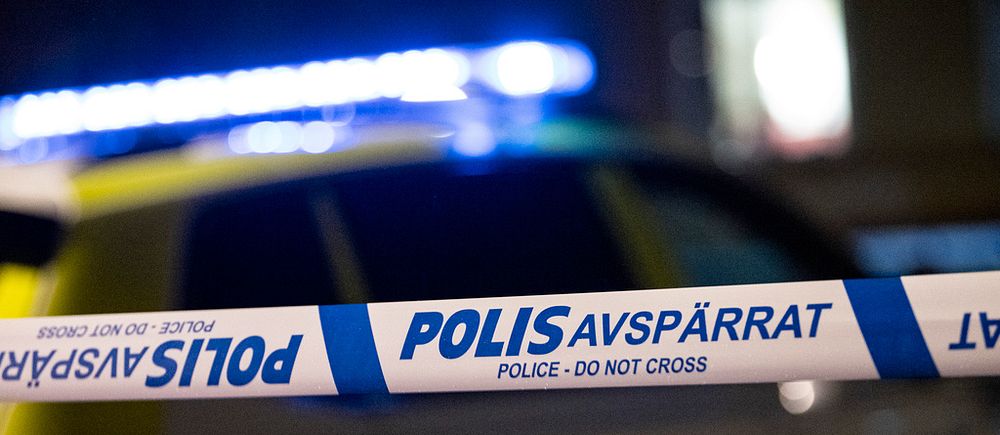avspärrningsband framför suddig polisbil med blåljus
