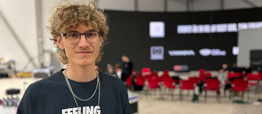 Person i t-shirt med hundtryck i väst, bakom en stolsrad och stor svart scen.