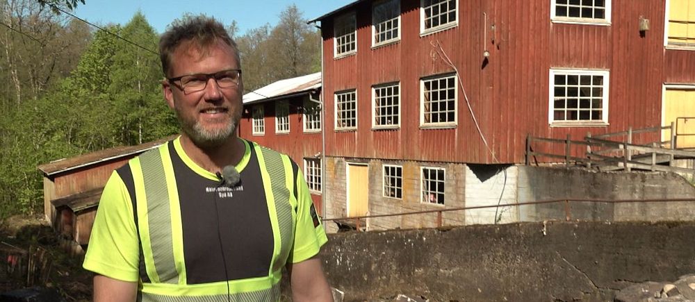 Person i varselväst står framför ett rött trähus vid en byggarbetsplats eller rivningsområde.