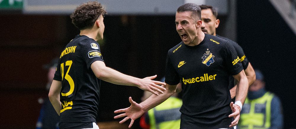 Två AIK-spelare på fotbollsplan med sträckta händer, publik och vakter i bakgrunden.