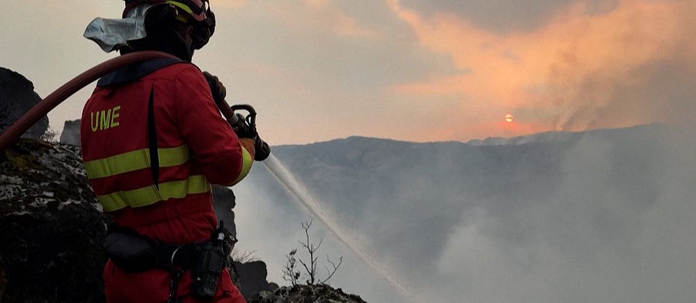 Brandman bekämpar skogsbrand i Spaniens norra och västra delar under rökig himmel.