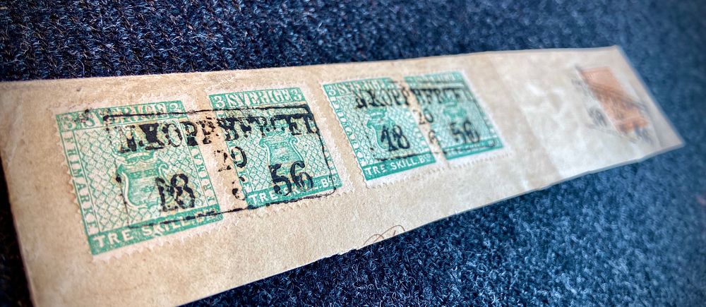Fyra svenska 3 shilling banco-frimärken från 1856 på ett kuvert mot en blå-svart bakgrund.