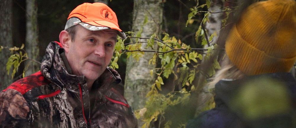 Anders Olsson, ordförande i Jägareförbundet Värmland. En man i orange keps och kamouflagekläder står vänd mot kameran och tittar på reportern som står i förgrunden med ryggen mot kameran.
