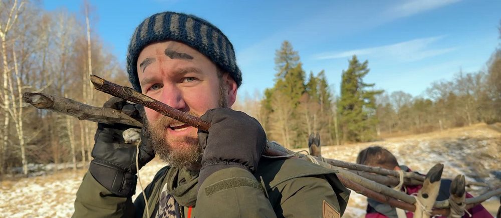 Två personer bär en hjort i en vintrig skogsmiljö med soligt väder.