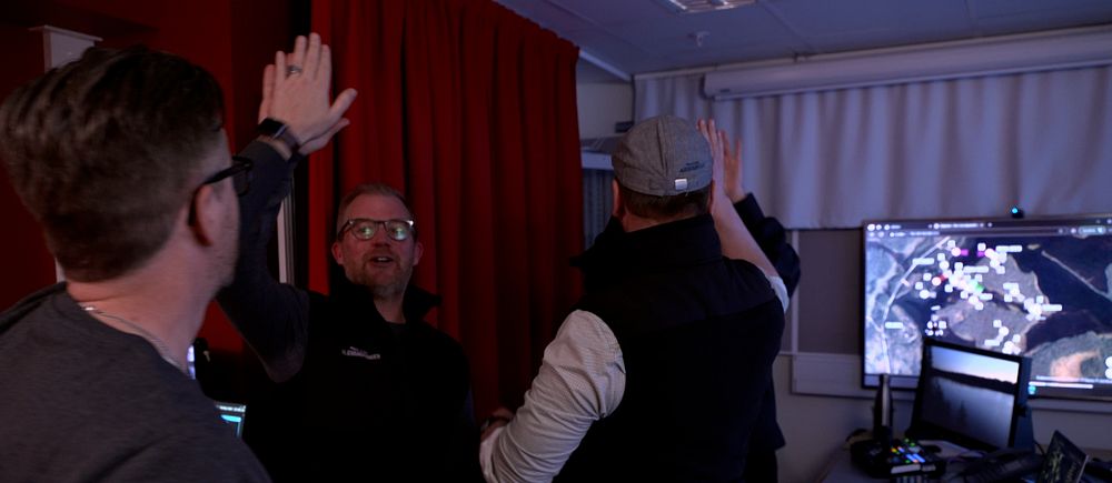 Flera personer ger varandra high five framför datorer i ett övervakningsrum.