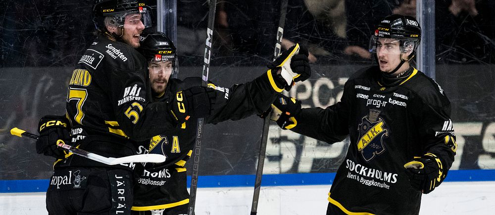 AIK-spelare firar efter mål på hockeyrink. Mörka tröjor och utrustning. Publik i bakgrunden.