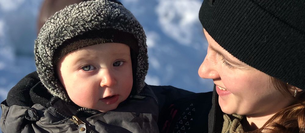 Moa Långdahl håller dottern Astrid klädd i vinterkläder på en snötäckt plats.