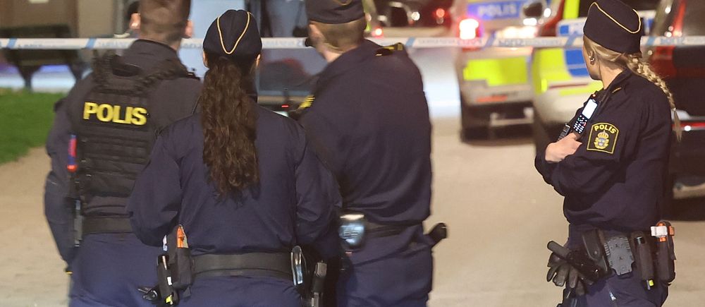 Fyra poliser står vid avspärrning, polisfordon med blåljus syns i bakgrunden.