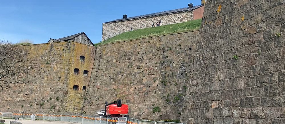 Ringmur och byggnad med avspärrningar i Varberg fästning. Klarblå himmel i bakgrunden.