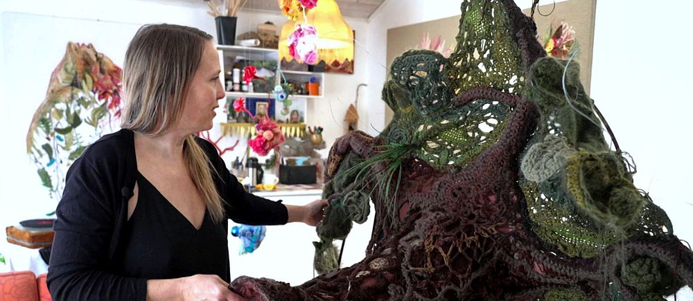 Kvinna visar detaljer från sin konstskulptur i ett färgglatt rum.