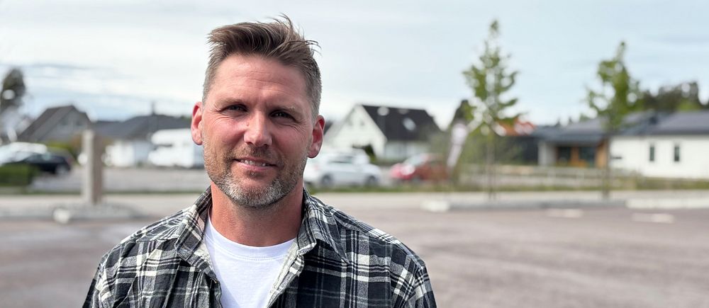 Person i rutig skjorta står på en tom parkering med hus i bakgrunden.