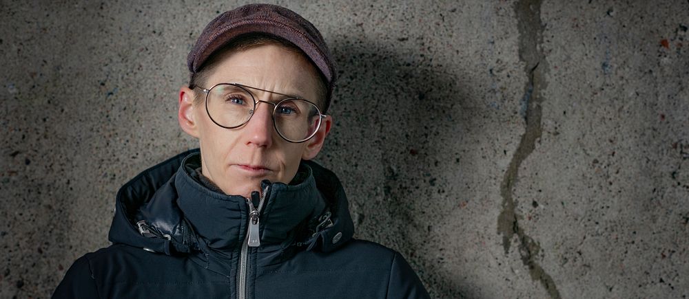 Person i mörk jacka står mot en grå betongvägg med spricka.