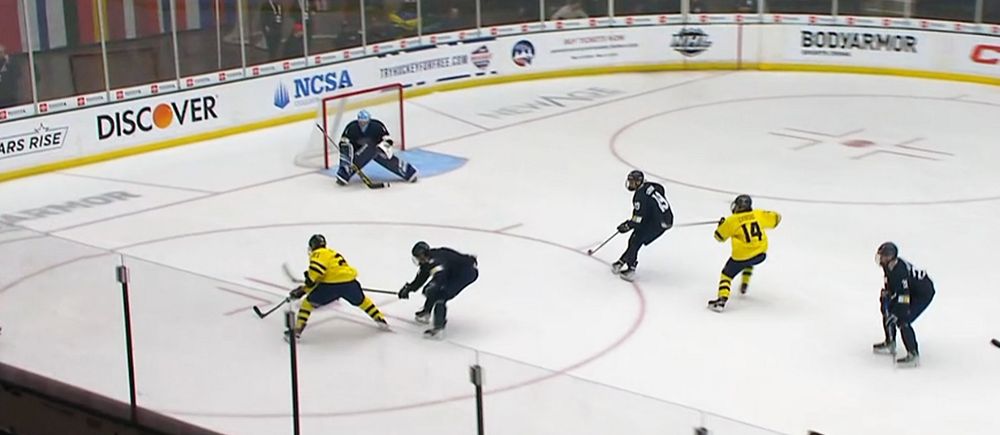 Ishockeyspelare i gul tröja skjuter mot mål, försvarare och målvakt försöker stoppa pucken.