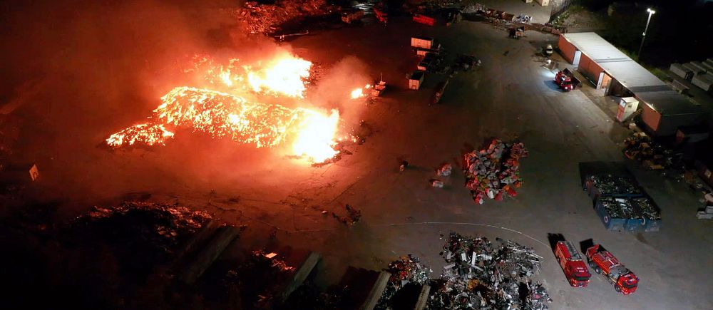 Stora lågor vid en brand på en återvinningscentral nattetid. Räddningstjänst på plats.