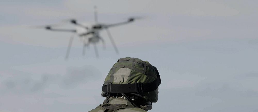 Soldat i uniform observerar en drönare som flyger i luften.