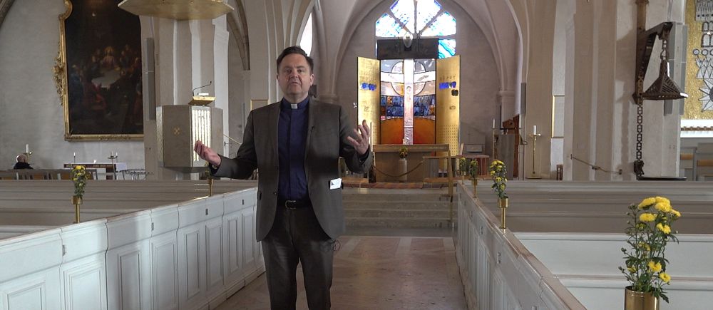 En präst står i en kyrka och håller ut sina armar