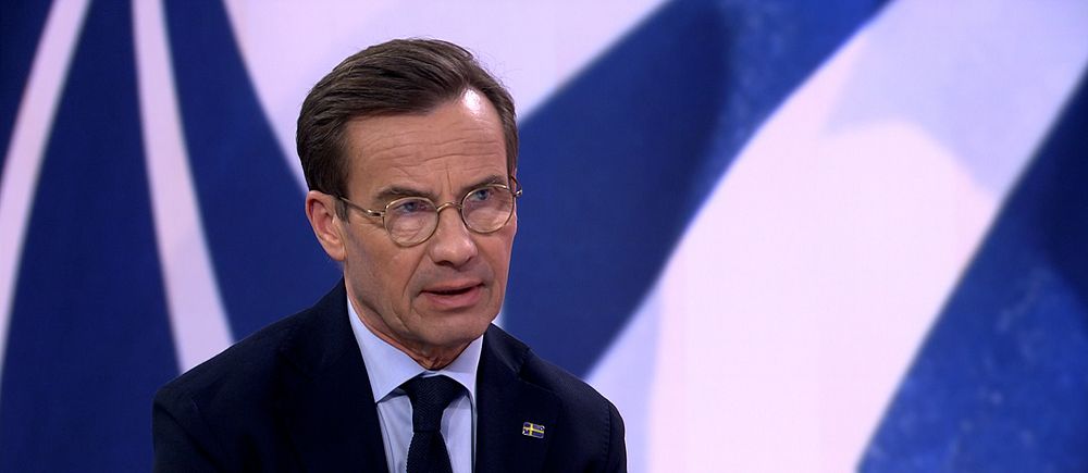 Person i kostym med NATO-logotyp som bakgrund.