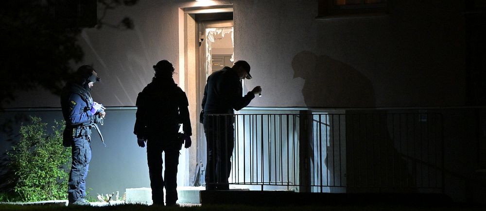 Poliser undersöker en bostadsingång i mörker med ficklampor.