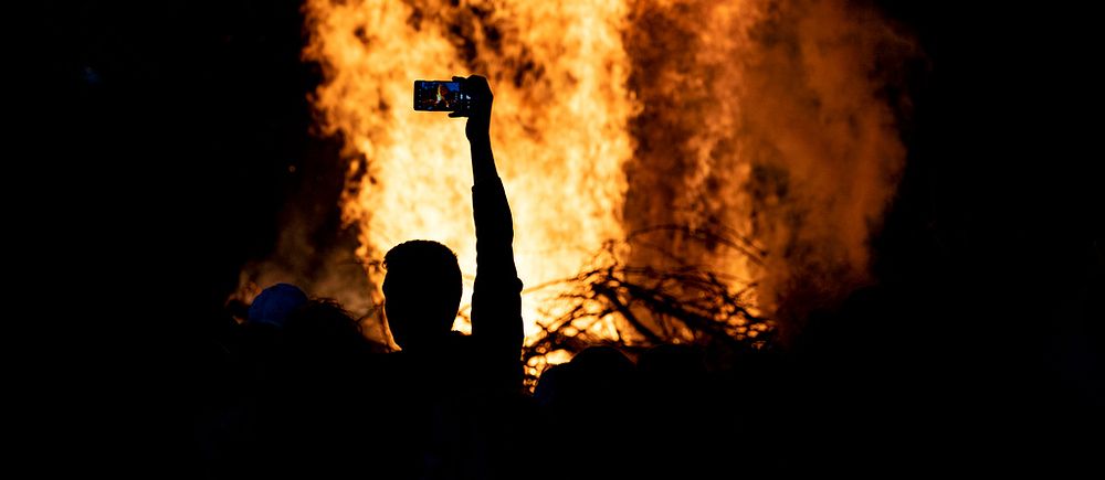 En majbrasa brinner kraftigt och en person filmar med sin mobilkamera.