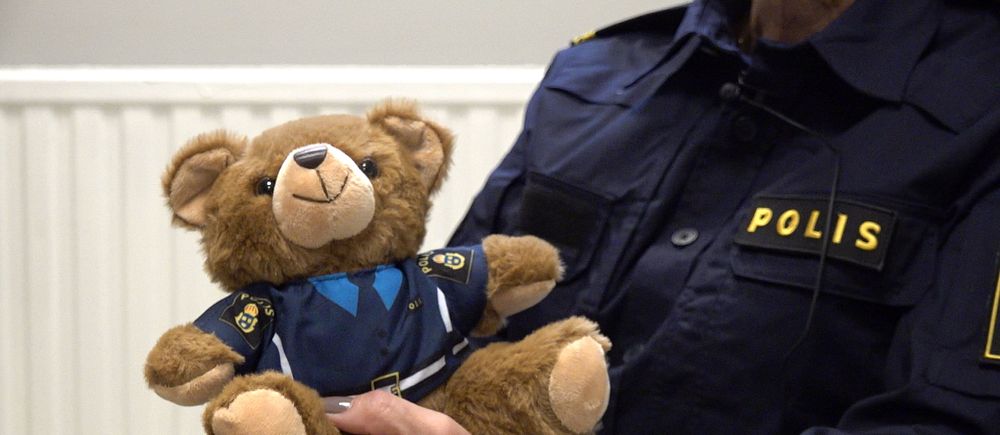 Polis håller i en liten nallebjörn. Båda har likadana polisuniformer.