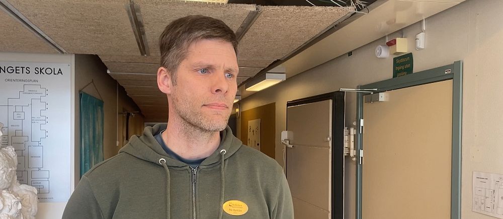 En person står i en korridor inomhus med vita dörrar och anslagstavla.