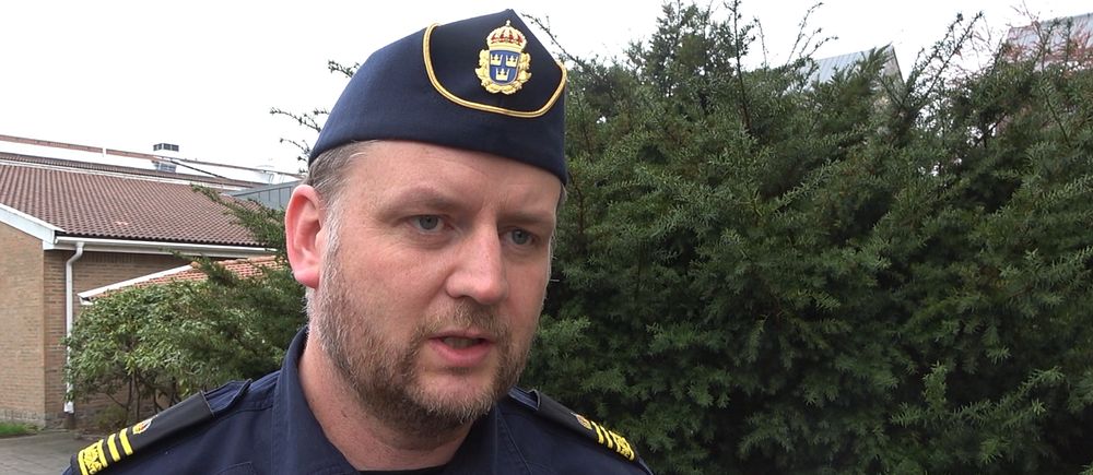 En polis står framför ett buskage i en utomhusmiljö.