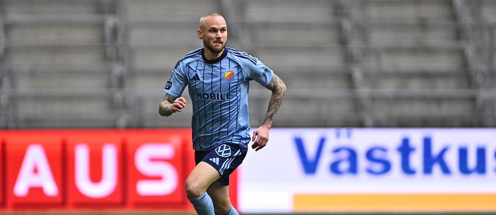 Fotbollsspelare i blått matchställ springer med bollen på en tom arena.