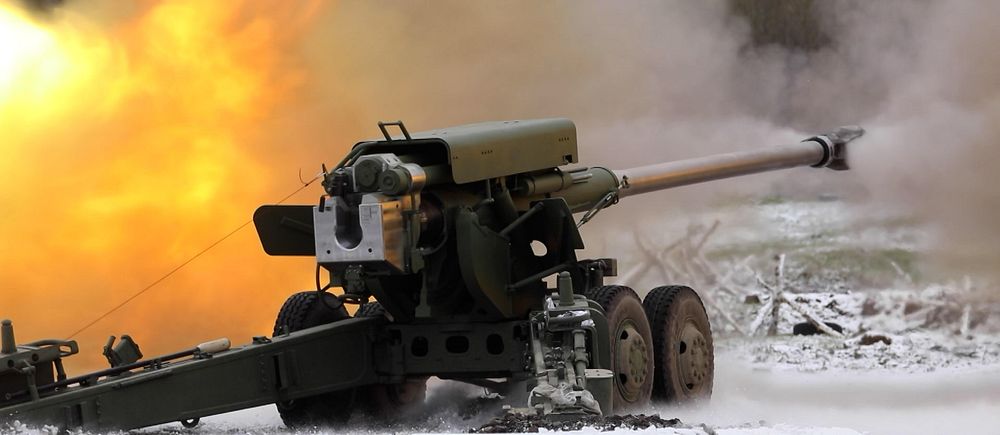 Artilleri avfyrar med eld och rök i bakgrunden på ett snötäckt fält.