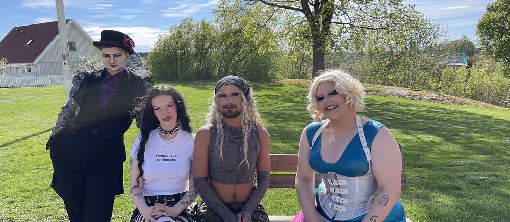Fyra personer med alternativa klädstilar sitter utomhus på en bänk i en park.