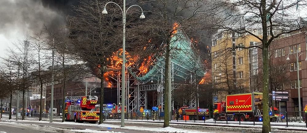 Brand i byggnad, brandbilar och blåljuspersonal på plats i snöigt stadsområde.