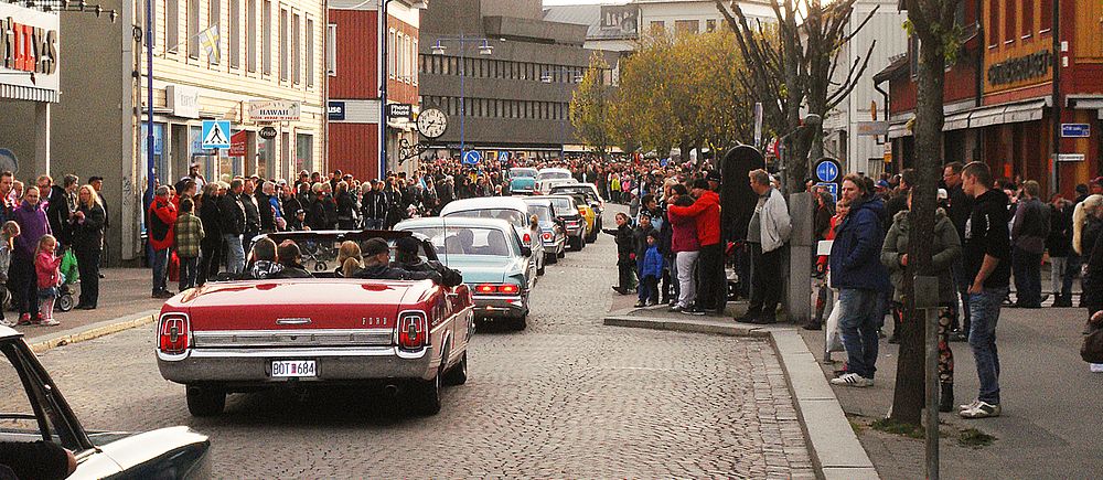 Bilkorteg med veteranbilar kör genom stadsgata, åskådare står längs trottoarerna.