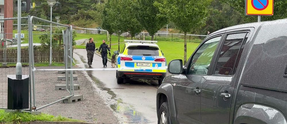 Polisbil vid avspärrning, två personer går mot den, grå SUV i förgrunden.