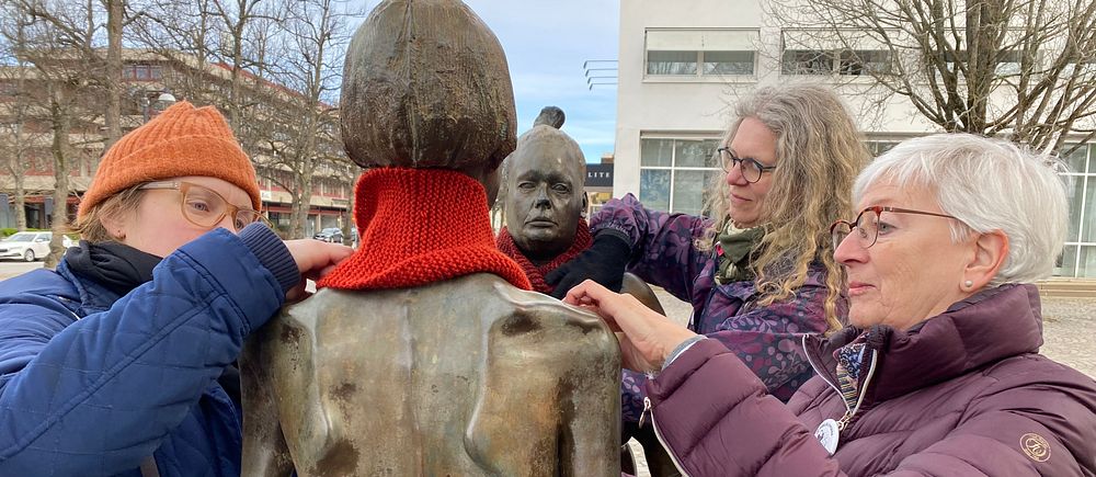 Kvinnor knyter röda halsdukar runt statyer
