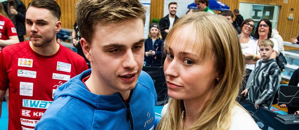 En sporthall med många människor, ett par står i centrum omgivna av publik och idrottare.