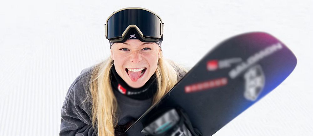 Person i vinterkläder håller en snowboard med varierande färger på skidbacken.