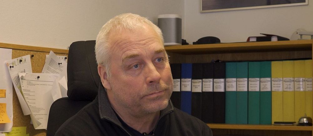 Person sitter i kontor med hyllor fyllda med mappar i bakgrunden.