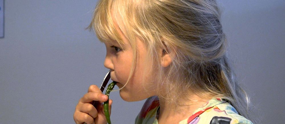 En flicka i profil som sitter och äter en grön böna.