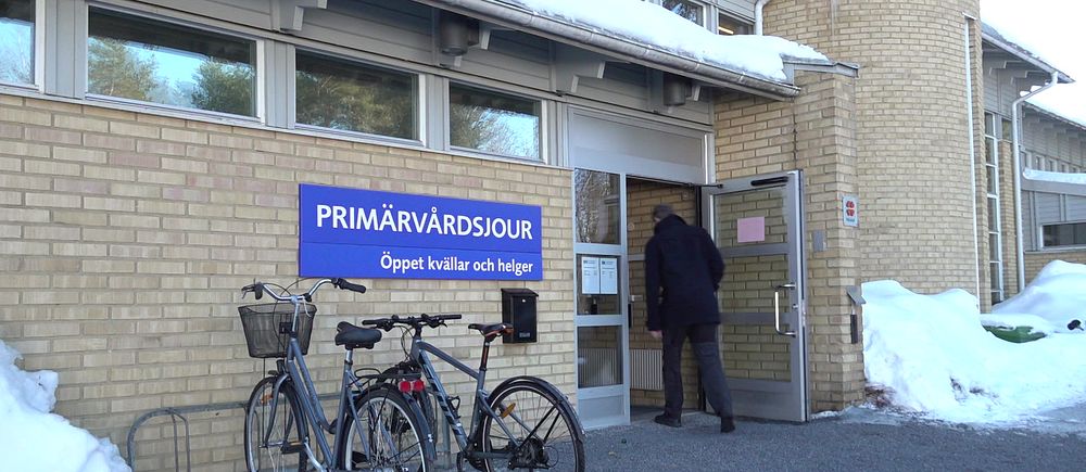 entrén till primärvårdsjouren i Umeå, en gul tegelbyggnad, en blå skylt med öppettider, en man som går in genom dörren