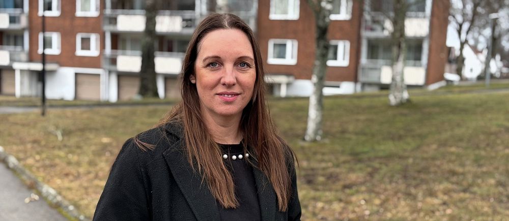 Person står utomhus framför tegelhus och grönområde.