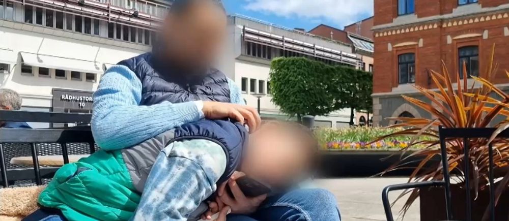 Två personer sitter nära varandra utomhus på en bänk med oskarpa ansikten.